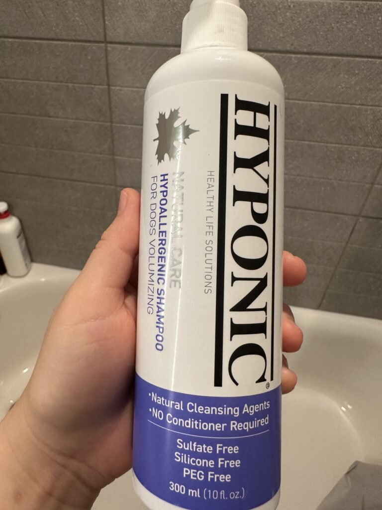 A hand holding a bottle of HYPONIC Hypoallergenic Shampoo for Dogs, Volumizing, 300 ml, with a purple label