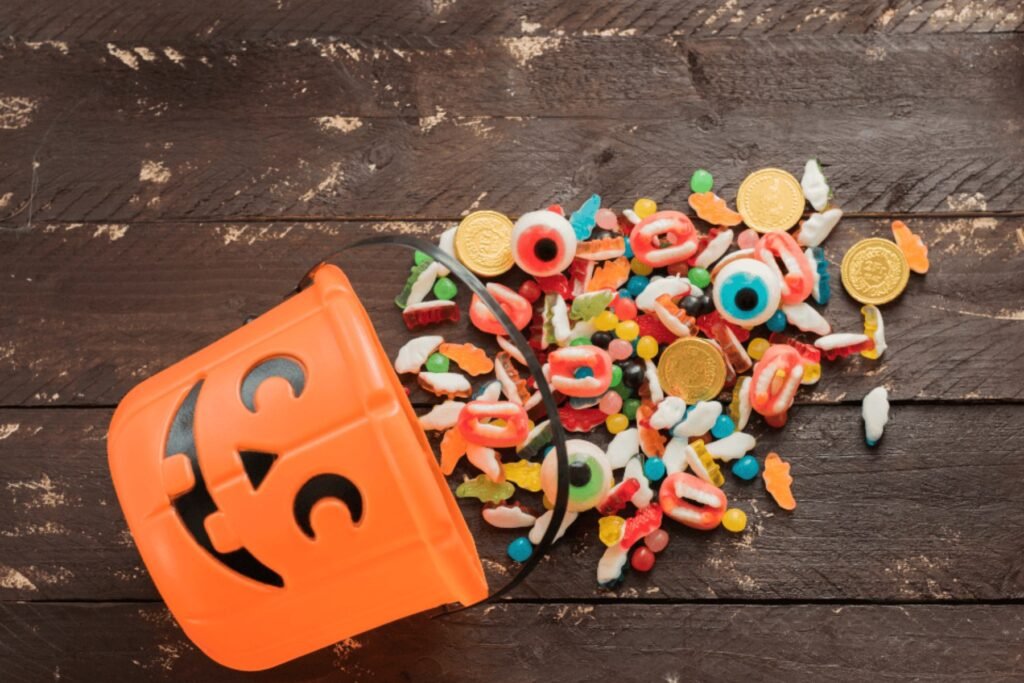 An orange jack-o’-lantern candy bucket spilling colorful candy across a wooden table